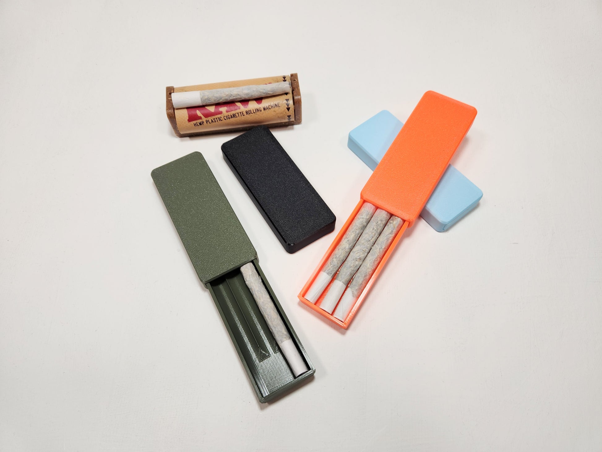Collection of smoking accessories including a rolling machine, papers, and cases on a light gray background.