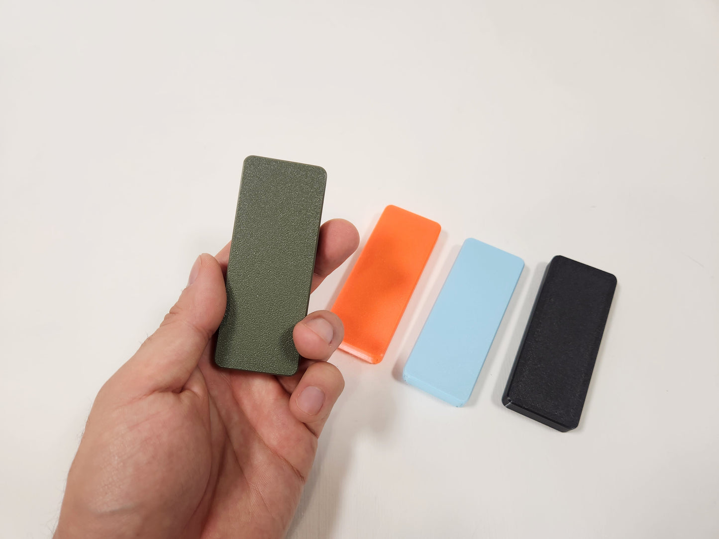 Hand holding a olive green case with three other colored cases on a white background